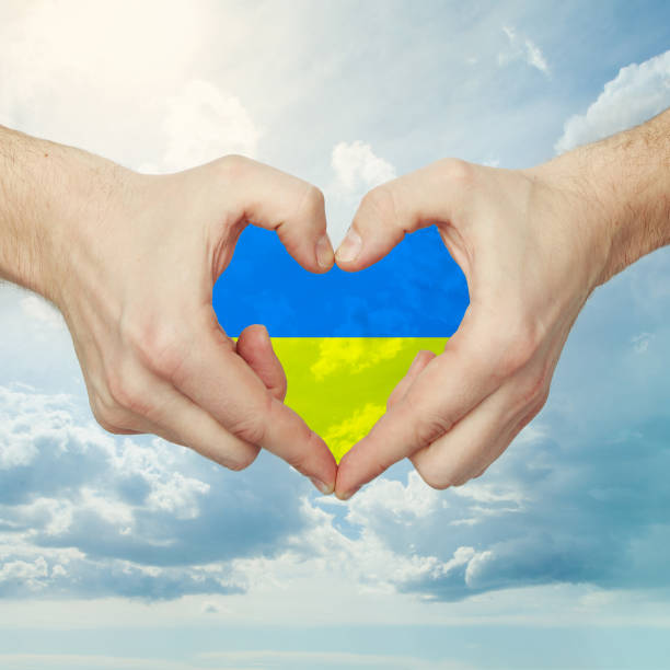 istock Male hands making heart shape with Ukrainian flag against sky clouds background 1392367894