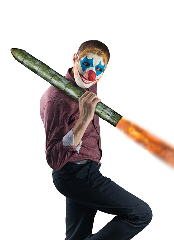 Nuclear missile in the hands of a clown. The concept of weapons in dishonest hands. Masked man isolated on white background.