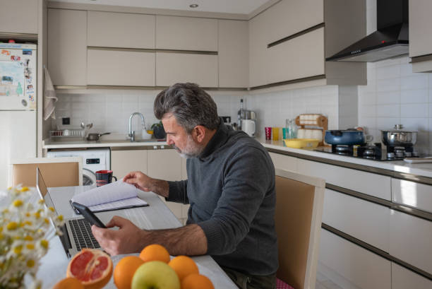 istock Shot of a mature man using a laptop while going through paperwork at home 1392374029