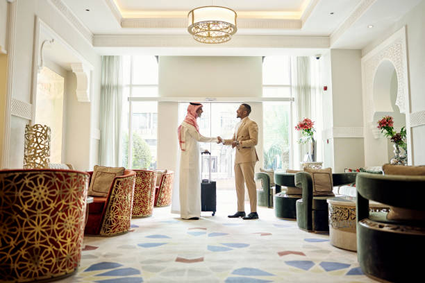 Saudi businessman shaking hands with client in hotel lobby Full length side view of mature professional in dish dash, kaffiyeh, and agal concluding a positive discussion with mid adult Black associate in western attire. arabian peninsula stock pictures, royalty-free photos & images