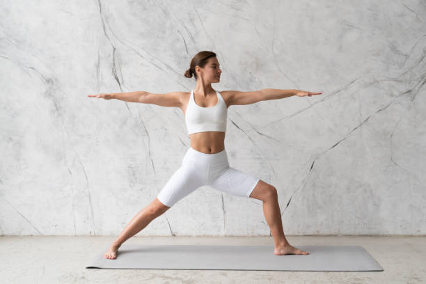 istock Young woman practicing yoga Warrior pose, Virabhadrasana against texturized wall 1392376443