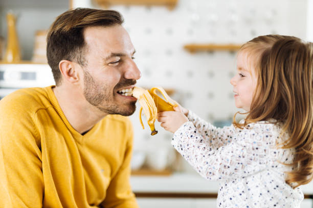 부엌에서 바나나로 아버지에게 먹이를주는 어린 소녀 - domestic kitchen father eating child 뉴스 사진 이미지