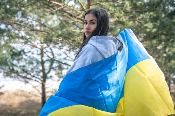 A young woman wrapped in the flag of Ukraine on a blurred background. A young woman wrapped in the flag of Ukraine on a blurred background of the forest. ukrainian language stock pictures, royalty-free photos & images