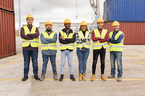 Multi-ethnic men and women working at shipping port with containers in background, logistics group