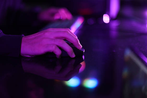 istock Close-up of a man's hand using a colorful computer keyboard playing an online game in a room with purple and multicolored neon lights. 1392385786