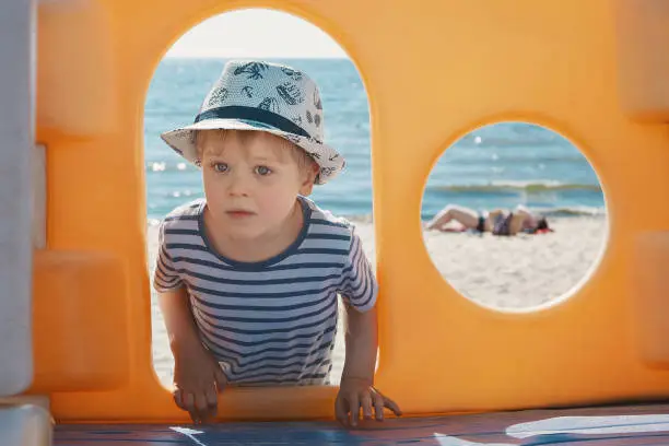 Portrait of a boy with a hat, framing with orange arche and a circle, beach in the background