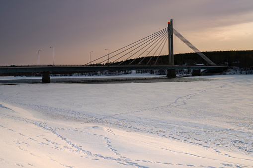A bridge over the frozen, footprint covered, Kemijoki river, Rovaniemi, Finland, at dawn.