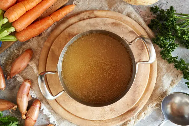 A pot of beef bone broth on table with vegetables, top view