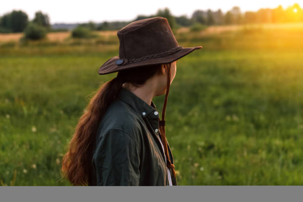 расфокусируйте молодую женщину в ковбойской шляпе. девушка в ковбойской шляпе в поле. заход солнца. природный фон. женщина смотрит в сторон� - side view southwest usa horizontal sun стоковые фото и изображения