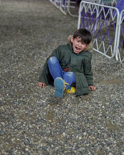 latin child sitting on the ground crying inconsolably with open mouth in wintertime outdoors with a green parka. concept of frustration in childhood - mouth open anger childhood outdoors imagens e fotografias de stock