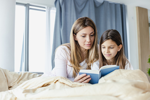 Young mother reading a book to her daughter in the morning