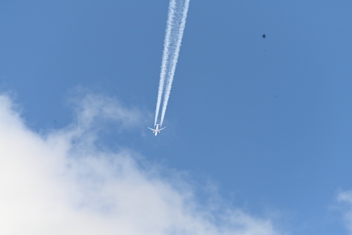 An aeroplane flying high across a blue sky with the vapour trails trailing behind from each of its engines, about to enter the fluffy white clouds with a bird flying behind it