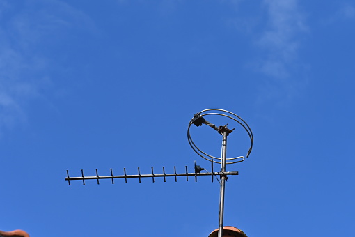 A circular and horizontal metal analogue aerial standing on the top of a chimney on the roof of a house with a crystal clear blue sky background