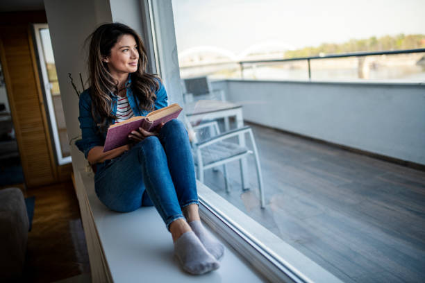 istock Woman reading a book, resting and looking through window 1392402932