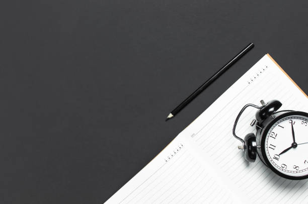 istock Flat lay black alarm clock, clean open notebook diary, pencil on gray dark background top view copy space. Concept time to work, desktop, Office desk, Minimalistic background for blog 1392404789