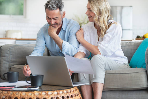 istock Mature couple using a laptop computer and doing paperwork on the sofa. 1392406549