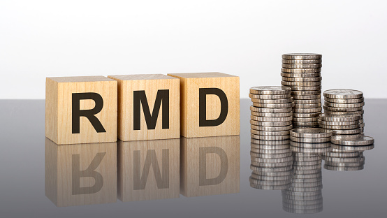 RMD - short for Required Minimum Distribution. wooden cubes. blocks lie on a black background. stacks with coins. inscription on the cubes is reflected from the surface of the table. selective focus.