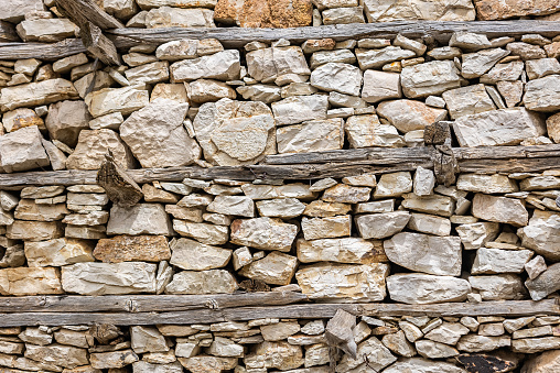 Ancient wall made of natural rocks with big white stone in the center and with plants between blocks as a background