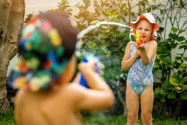 Photo of little girl and boy playing with water guns at garden on hot summer day. children having fun outdoors