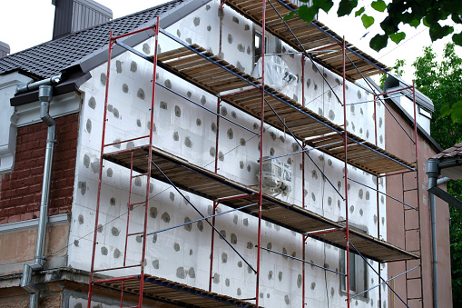 Building facade under renovation works with construction scaffolding frame. Wall insulation with styrofoam sheets for energy efficient home.