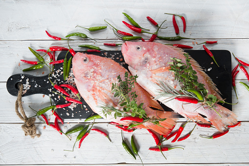 raw fresh pink tilapia fish lies on a board whith yellow lemon on white wooden planks. High quality photo