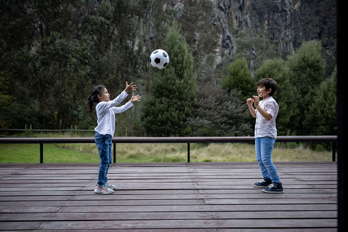 Happy Latin American kids playing outdoors with a ball on the deck of their house