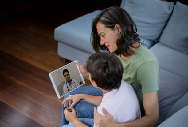 medico che parla con un giovane paziente a casa attraverso una videochiamata - consultant explaining computer home interior foto e immagini stock