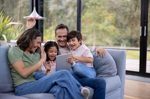 Happy Latin American family at home greeting some relatives on a video call and smiling while using a tablet - stay at home concepts