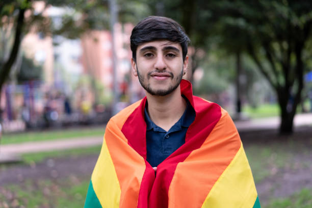 istock Young gay man with a rainbow flag over his shoulders facing camera cheerfully 1392444588