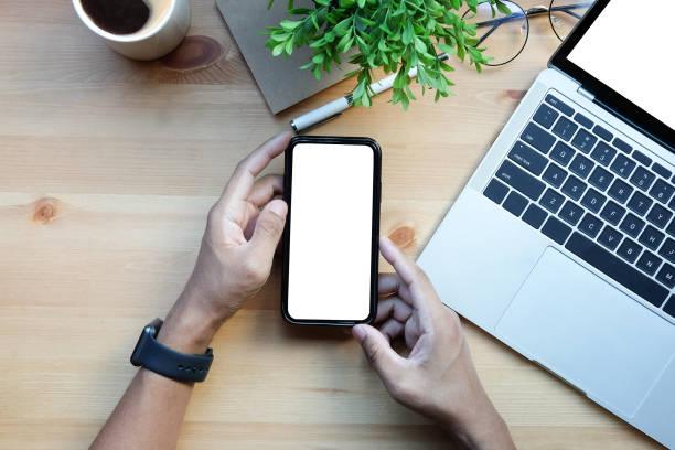 istock Above view man holding smart phone with white empty screen on wooden desk. 1392445409