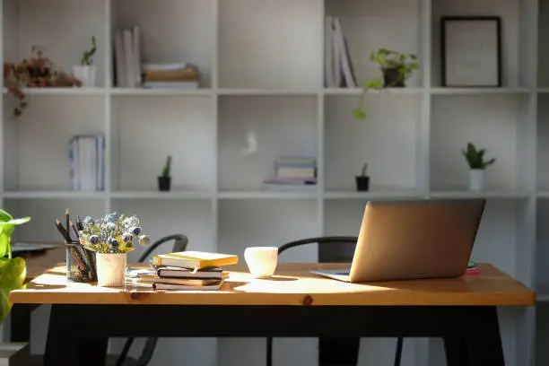 Photo of Bright modern office with computer laptop, houseplant and supplies on wooden table