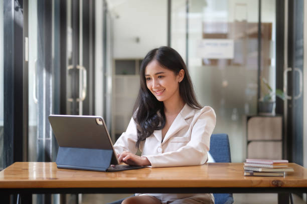 istock Confident asian business woman using computer tablet while sitting in bright modern office. 1392447385