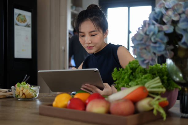 Woman sitting at kitchen table full of fresh vegetables and searching recipes on digital tablet. Woman sitting at kitchen table full of fresh vegetables and searching recipes on digital tablet. nutritionist stock pictures, royalty-free photos & images