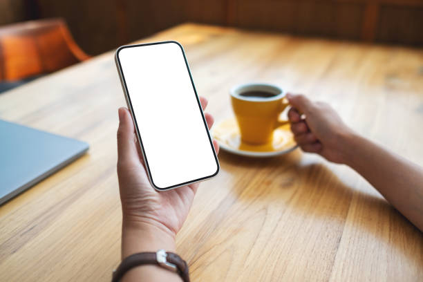 istock Mockup image of a woman holding mobile phone with blank desktop screen while drinking coffee 1392447725