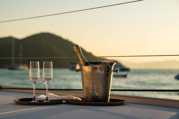 夏の日没時に海を航行する双胴船のシャンパングラス付きのアイスバケツのシャンパンボトル。 - sunset yacht luxury sailboat ストックフォトと画像