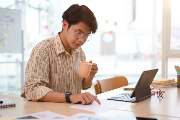 istock Focused Asian businessman sipping coffee while checking sale report 1392459276