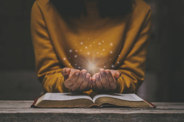 donna che prega sulla sacra bibbia al mattino hanno una luce gialla e scintille in arrivo. mano della donna con la bibbia che prega. crisi di vita cristiana preghiera a dio. - please god foto e immagini stock