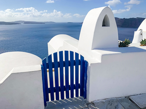 Small traditional wooden door on the island of Santorini. Closed blue wicket. View of caldera. Sunny day. Blue sky. Nobody.