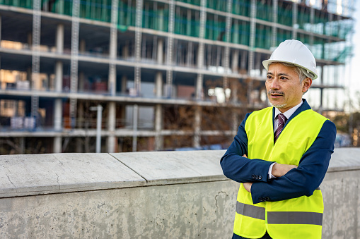 A portrait of a mature Japanese man, a civil engineer, who stands on the construction site and supervises the works