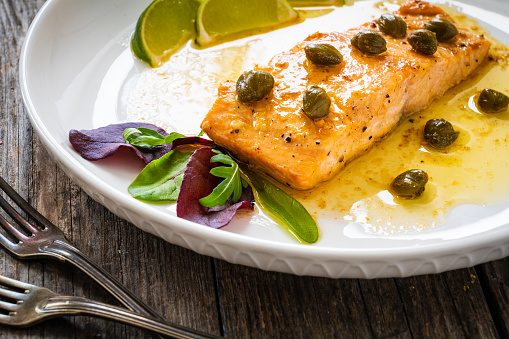 Butter sauce fried salmon steak with capers and lime on wooden table