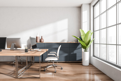 White industrial office interior with seats, pc computer on desk, side view, drawer with art decoration and plant, hardwood floor. Panoramic window on city view. Mock up black wall. 3D rendering