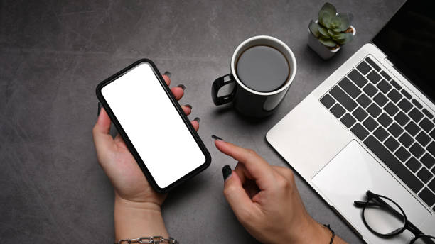 istock Woman hand holding mobile phone with blank screen on dark stone background. Top view. 1392472271