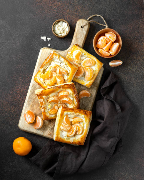 istock Mini puff pie with cheese cream, almonds, and tangerines in a plate on the kitchen table. Delicious layered square with citrus fruits, dorblue or ricotta, nuts on a culinary background top view 1392472557