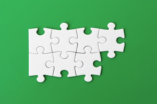 Seven white puzzle pieces on a green background. Merging different elements into a whole