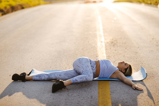 Beautiful young woman having work out on empty asphalt road on sunny summer day