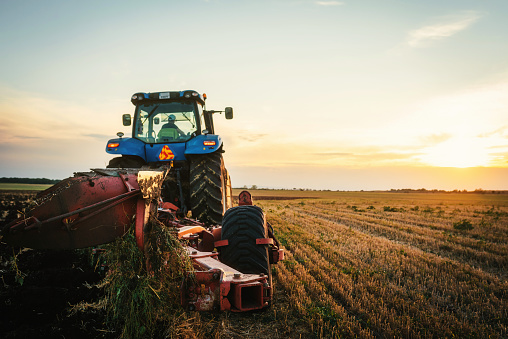 man making bales with tractor and machine in big field at sunset