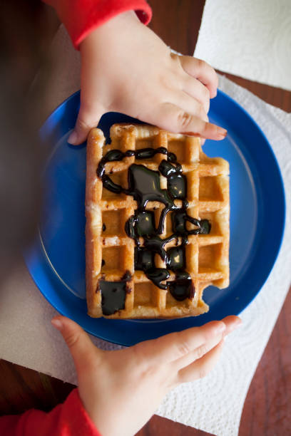 istock Child holds a waffle over blue plate 1392491211