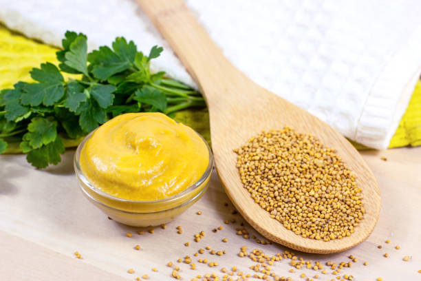 Yellow Dijon mustard sauce in glass dip with wooden spoon full of dry mustard seeds on the table in the kitchen Yellow Dijon mustard sauce in glass dip with wooden spoon full of dry mustard seeds on the table in the kitchen. dijonnaise stock pictures, royalty-free photos & images