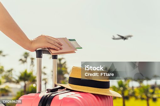 istock Woman with pink suitcase and passport with boarding pass standing on passengers ladder of airplane opposite sea with palm trees. Tourism concept 1392494719
