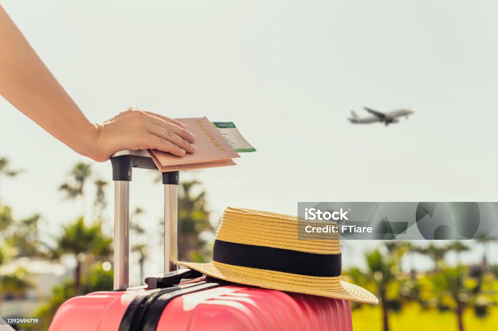 Woman with pink suitcase and passport with boarding pass standing on passengers ladder of airplane opposite sea with palm trees. Tourism concept Vacations Stock Photo